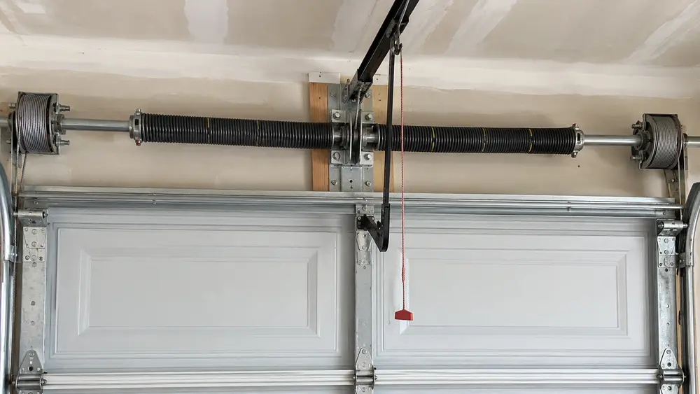 Technician inspecting a matched pair of torsion springs above a residential garage door